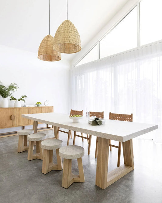 Modern dining area with a white table, wooden chairs, and stools in a bright room.