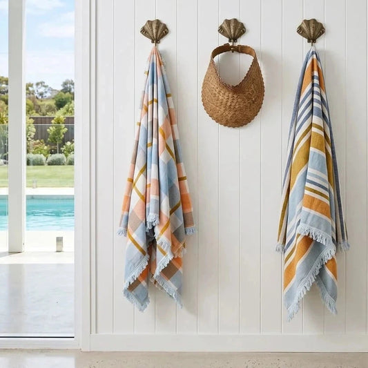 Two patterned towels hanging on hooks with a view of a pool outside.