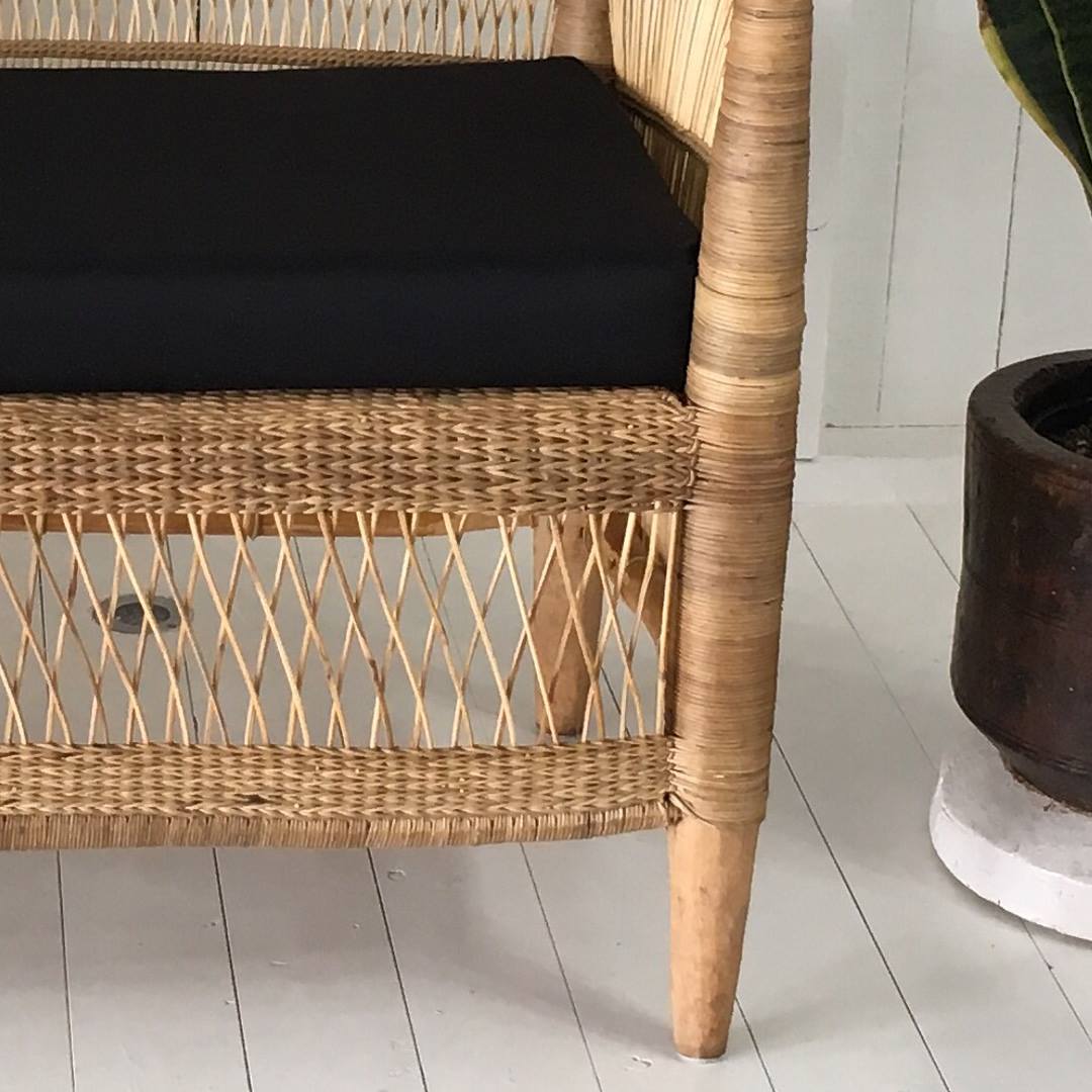 Wicker chair with a black cushion on a white wooden floor.