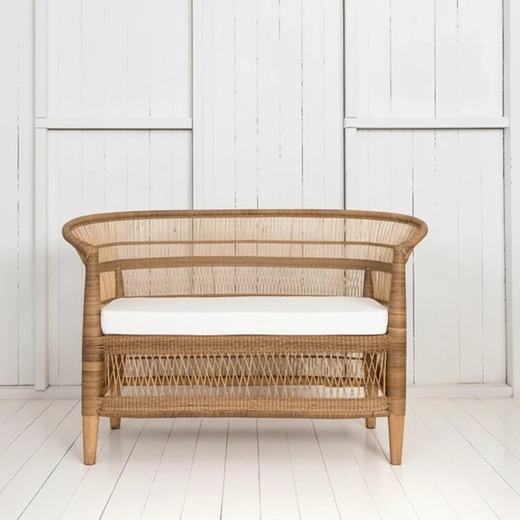 Wicker chair with white cushion next to a potted plant on a white wooden floor.