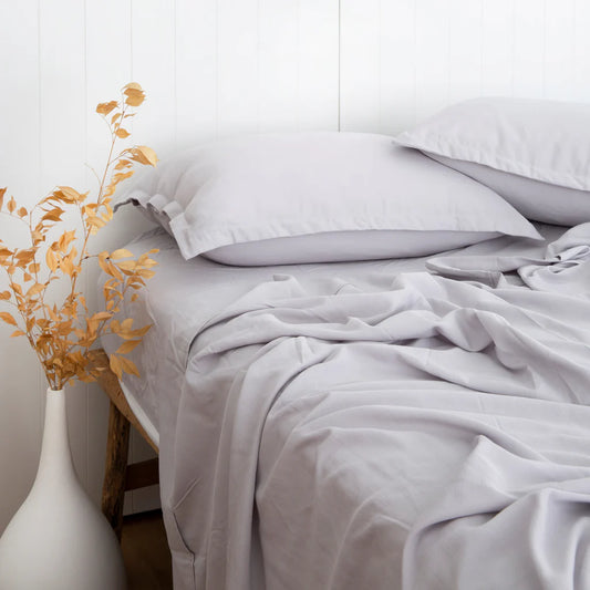 Neatly made bed with white bedding and a vase with yellow leaves on a white background