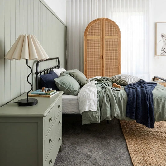 Bedroom with a bed, nightstand, and lamp, featuring a wicker headboard.