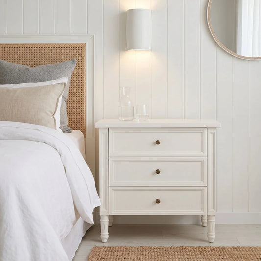Bedroom with a bed, nightstand, and lamp against a white paneled wall.