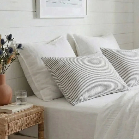 Bedroom with white bedding, striped pillows, and a small table with a vase and glass.