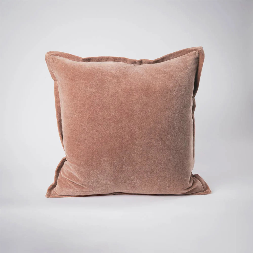 A square throw pillow in a dusty rose velvet fabric, photographed against a neutral light gray studio background.