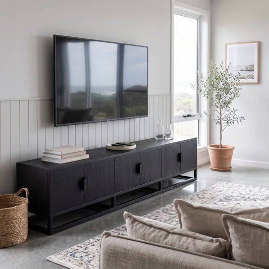 A modern black wooden media console with cabinet doors and open shelving, styled in a bright living room under a wall-mounted flat-screen TV. The console is decorated with books and small glass vases, set against white wainscoting on a light gray wall.