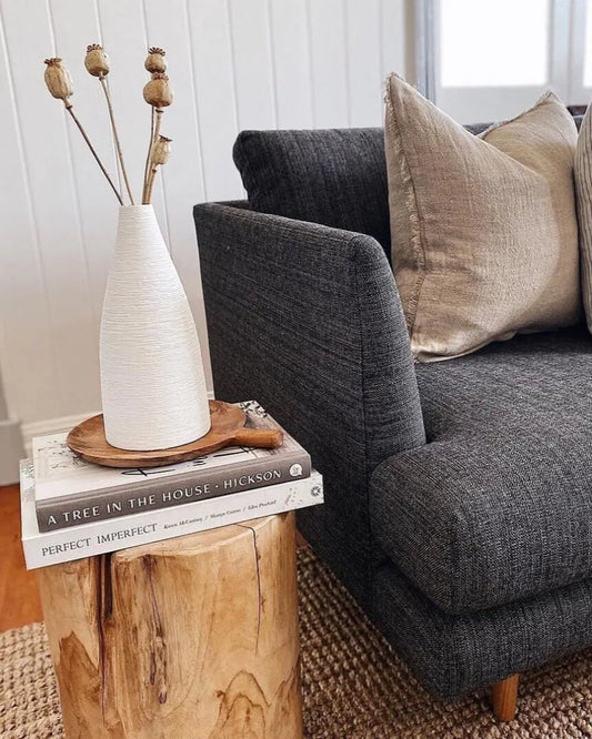 Gray sofa with decorative cushions next to a teak stump side table with a vase and books.