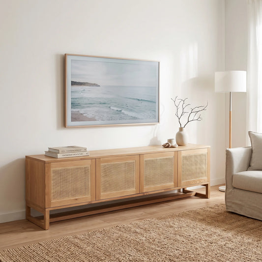 A light natural wood sideboard with woven cane panel doors, styled in a bright, modern living room under a framed ocean landscape print.
