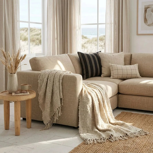 Beige sectional sofa with throw blanket and pillows in a bright living room.