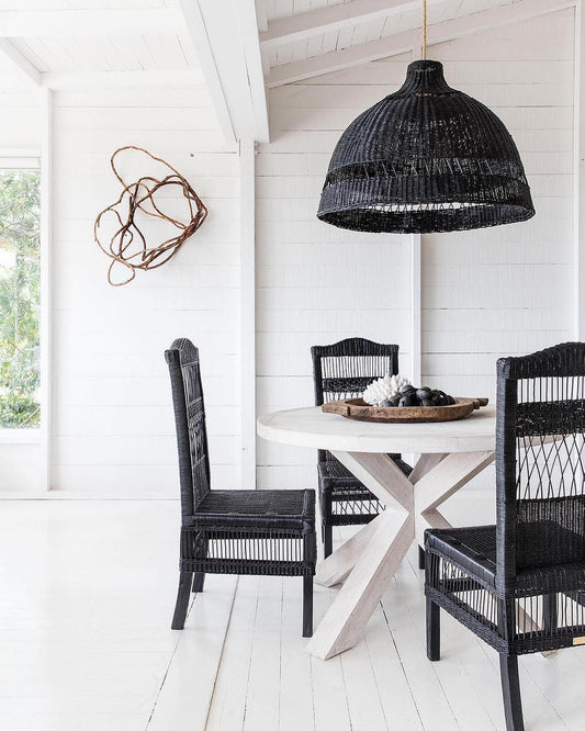 Dining area with black wicker chairs and a round table under a black woven pendant light.