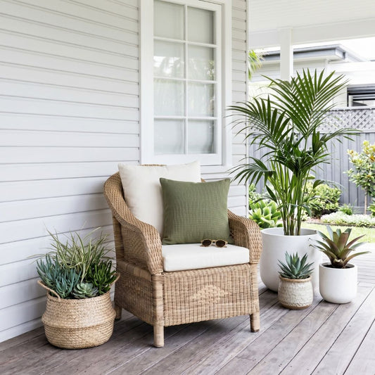 Wicker chair with cushions on a wooden deck, surrounded by potted plants.