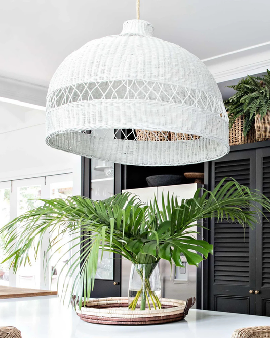 White woven pendant light hanging above a table with plants in a modern interior setting.
