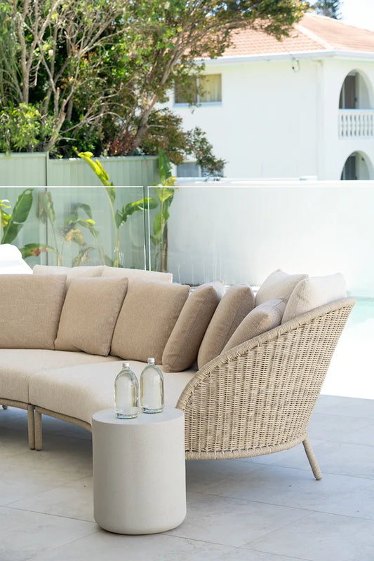 Outdoor patio setting with a beige sectional sofa and wicker chair, accompanied by a small round table.