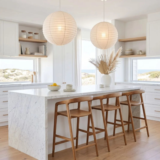 Modern kitchen with marble island, wooden bar stools, and white round linen pendant lights.