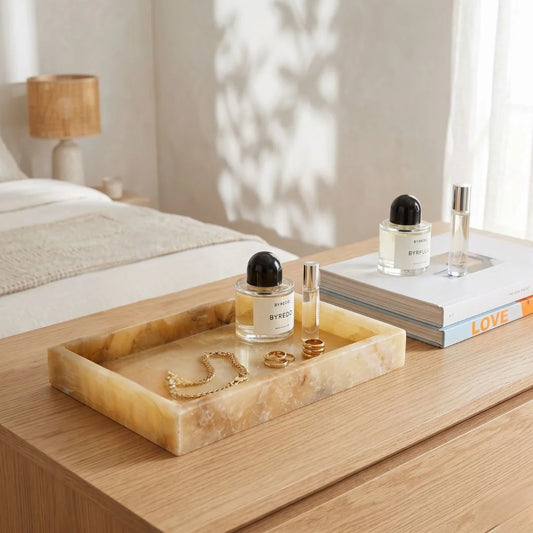 Decorative natural onxy tray with perfume bottles, jewelry, and books on a wooden surface.