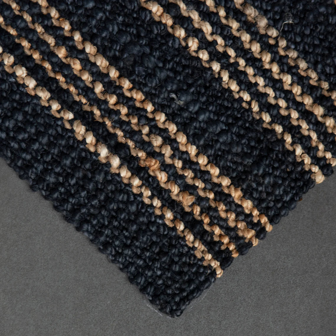 Close-up of a textured black and beige rug corner on a gray background