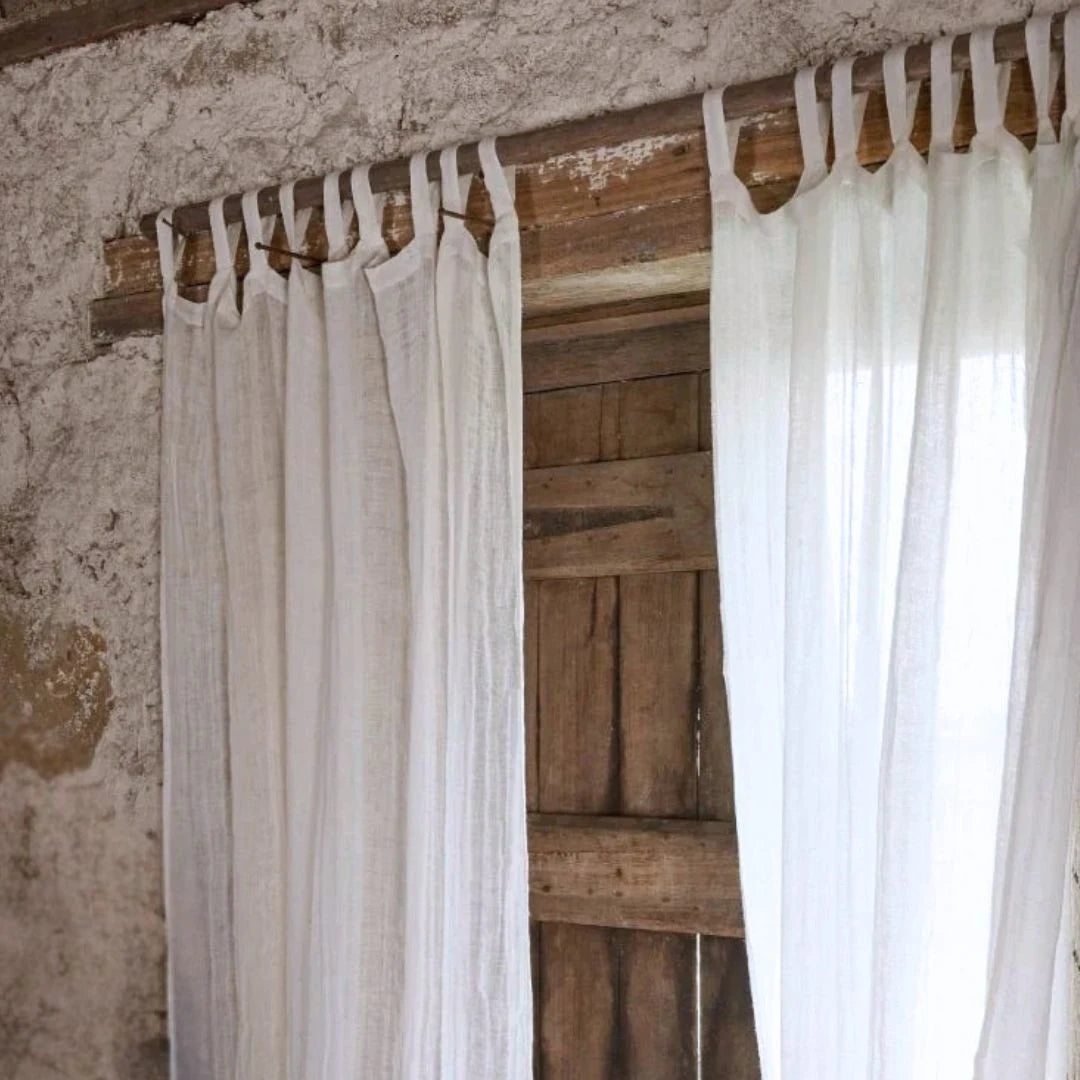 White curtains hanging on a wooden rod against a rustic wall.
