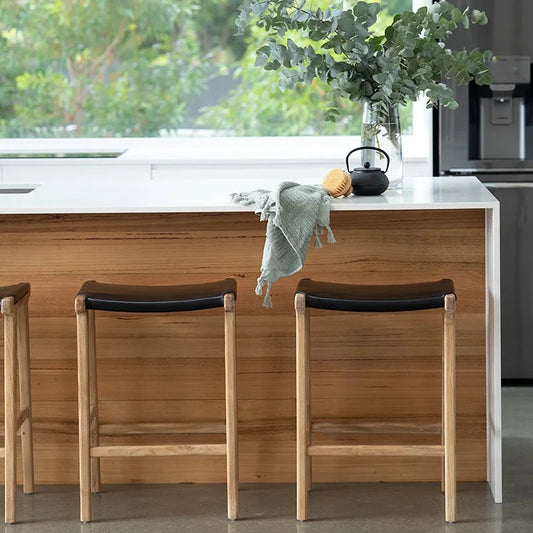 Modern kitchen with wooden island and stools, featuring a window view of greenery.