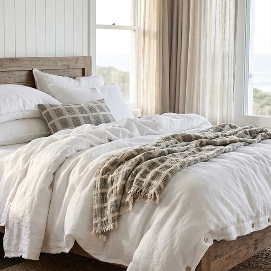 Neatly made bed with white bedding and plaid blanket in a bright bedroom.