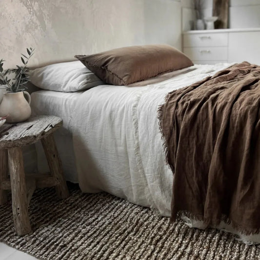 Bedroom with a bed featuring brown and white bedding, a wooden stool, and decorative items.