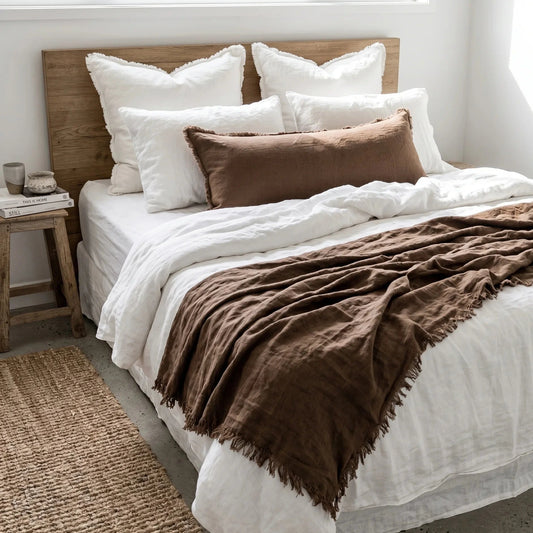 Bedroom with a bed featuring white bedding and brown throw blanket, wooden headboard, and side table.