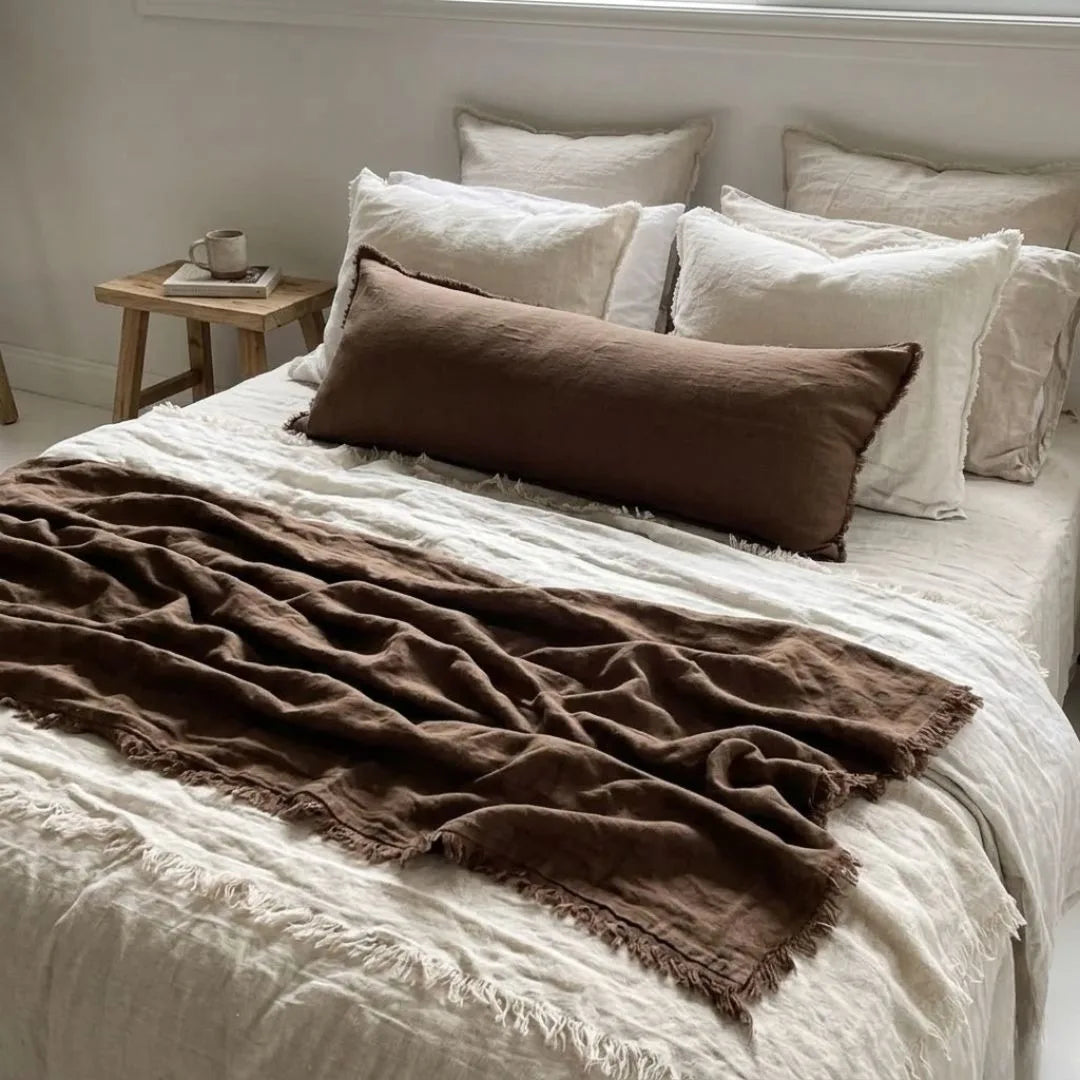 Bed with brown throw blanket and white pillows in a bedroom setting.