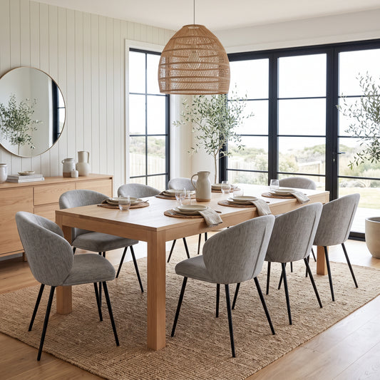 A modern dining room set featuring a light oak rectangular table and eight gray upholstered chairs with black metal legs, arranged on a natural jute rug under a woven pendant light.