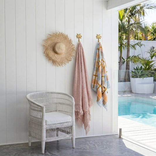 Wicker chair with a straw hat and beach towels by a poolside.