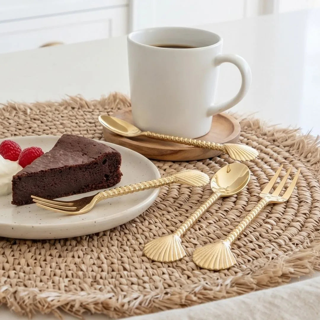 White mug with a slice of chocolate cake and gold spoons on a woven mat.