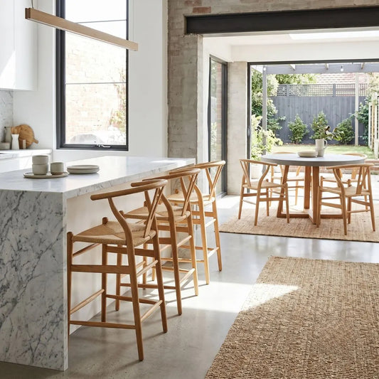Modern kitchen with marble island, wooden bar stools, and dining table.