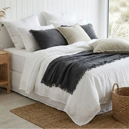 Neatly made bed with white bedding and gray throw blanket in a bright bedroom.
