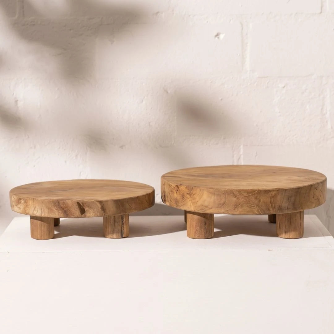 Two round wooden stools with thick natural wood tops and short block legs, displayed on a white surface against a white brick wall.