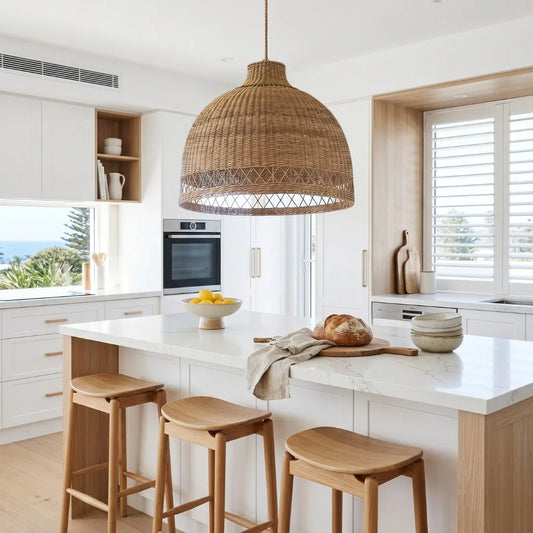 Modern kitchen with white countertops, wooden stools, and a oversized woven cane pendant light.