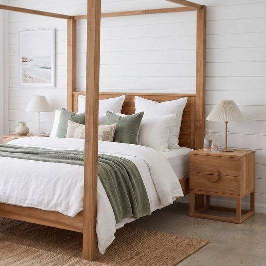 A light natural wood four-poster bed with white bedding, sage green pillows, and a sage green throw blanket, styled in a bright, modern bedroom with white shiplap walls, matching wood nightstands, and lamps.