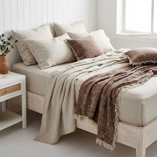 Neatly made bed with beige and brown bedding in a bright bedroom.
