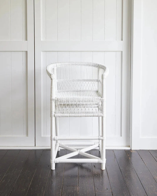 White wicker chair against a white paneled wall.