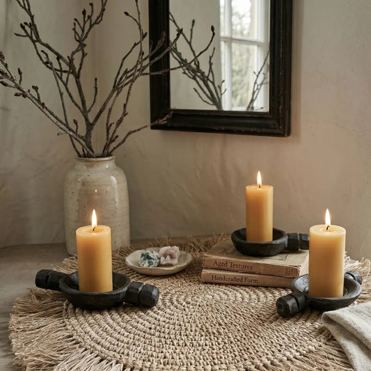 Candles in black holders on a woven mat with a vase of branches and mirror in the background.