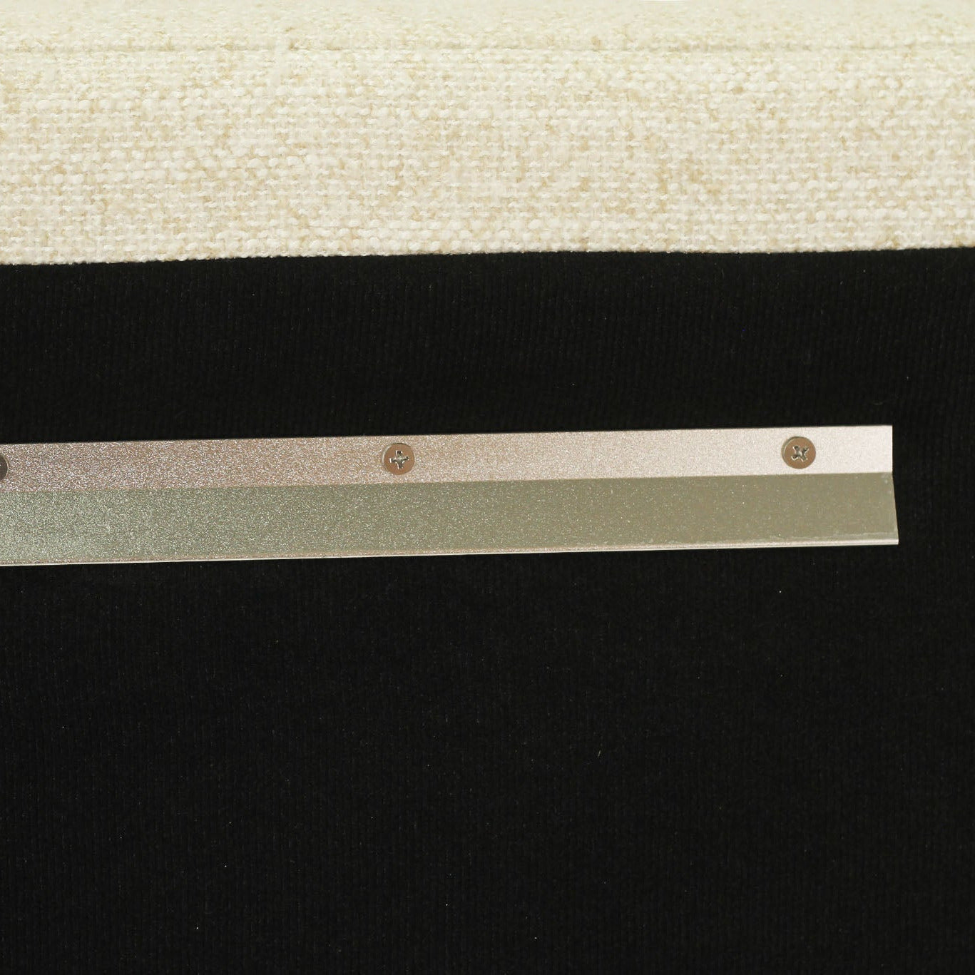 A close-up of a metallic silver strip with four small round screw-like details, positioned horizontally against a black background with a beige textured surface at the top.