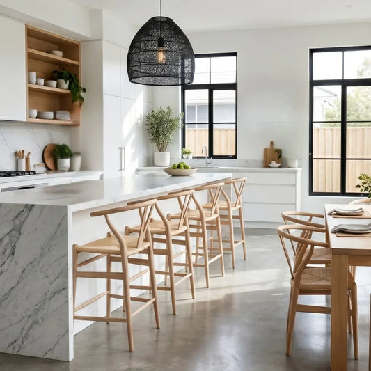 Modern kitchen with marble island, wooden chairs, and large windows.