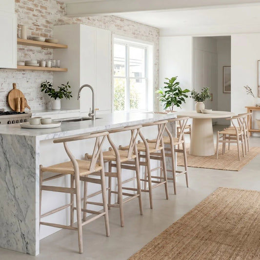 Modern kitchen with marble island and wooden stools, light wood cabinets, and white walls.