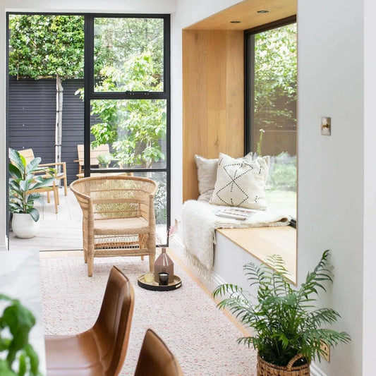 Modern living room with Sun Republics Malawi cane chair, sofa, and large windows overlooking greenery.