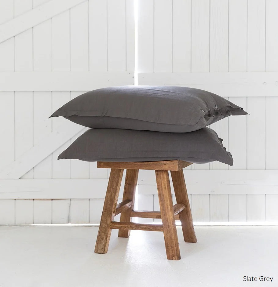Two slate grey pillows stacked on a wooden stool against a white paneled wall.