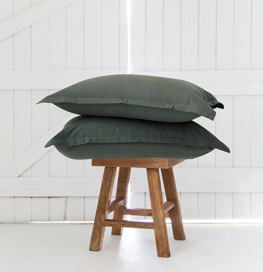 Two green pillows stacked on a wooden stool against a white paneled wall.