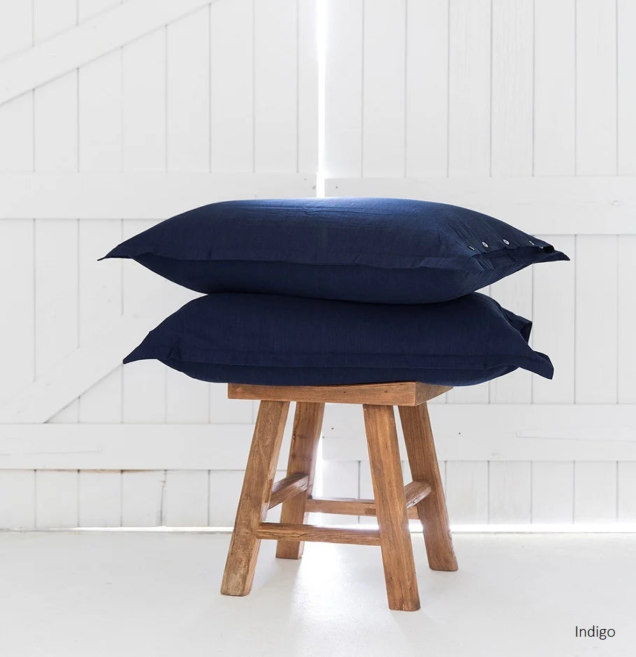 Two navy blue pillows stacked on a wooden stool against a white paneled wall.