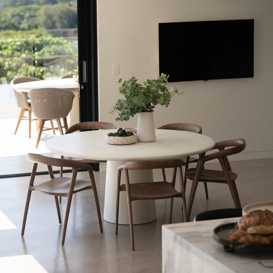 Modern dining area with a round table and chairs, featuring a television on the wall.