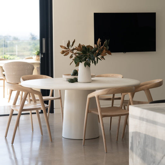Modern dining area with a white round table and chairs, featuring a television on the wall.