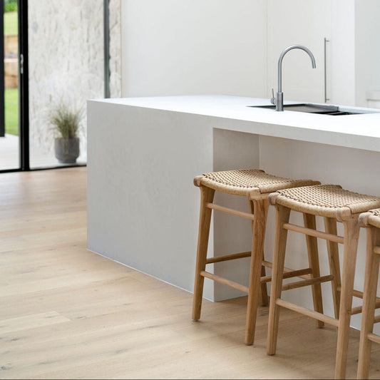 Modern kitchen with white island, wooden stools, and glass doors leading to a garden.
