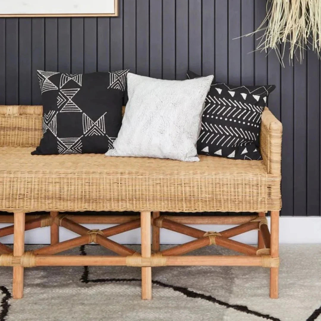 Wicker bench with patterned cushions against a dark paneled wall.