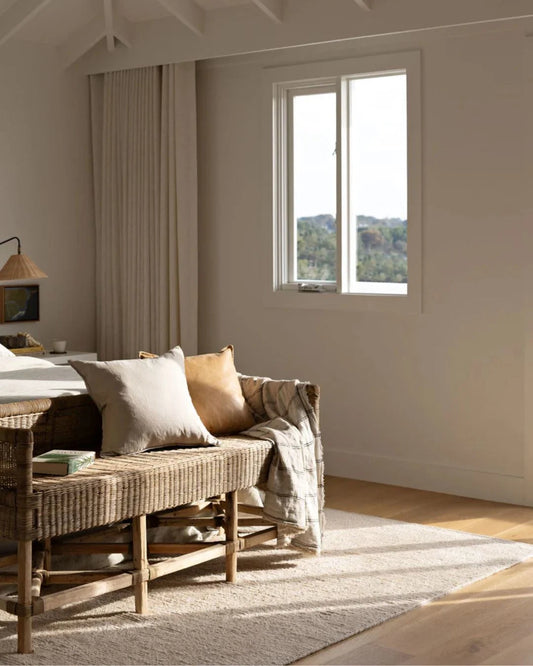 Cozy bedroom with a wicker bench, cushions, and a window view of greenery.