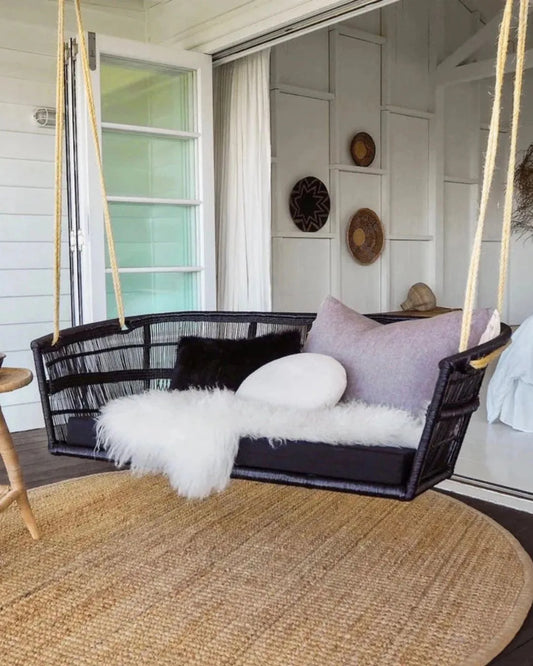 Black wicker swing with cushions on a porch with a round woven rug.